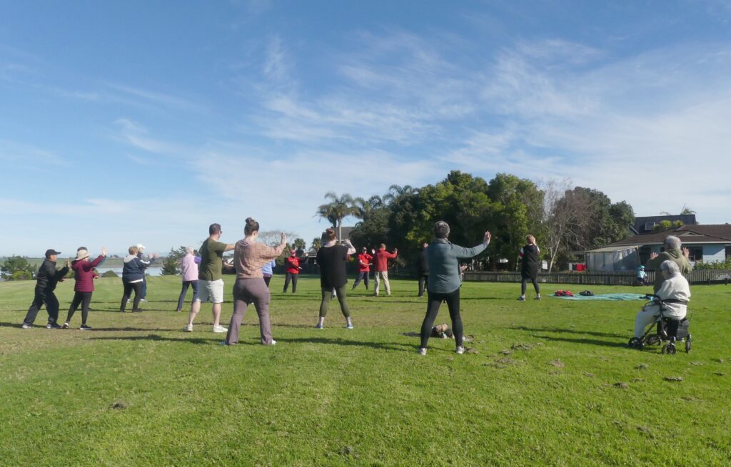 Group of people doing tai chi outside on green grass and with a blue sky above