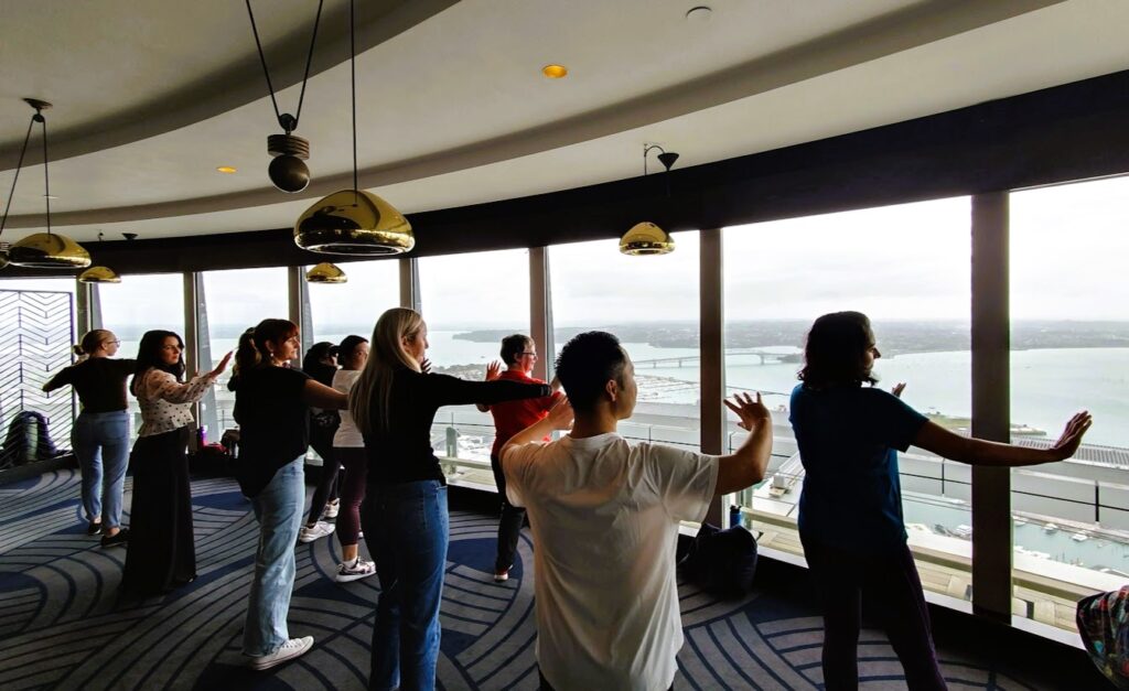 People doing tai chi with a view over the Waitemata Harbour and the Auckland Harbour Bridge